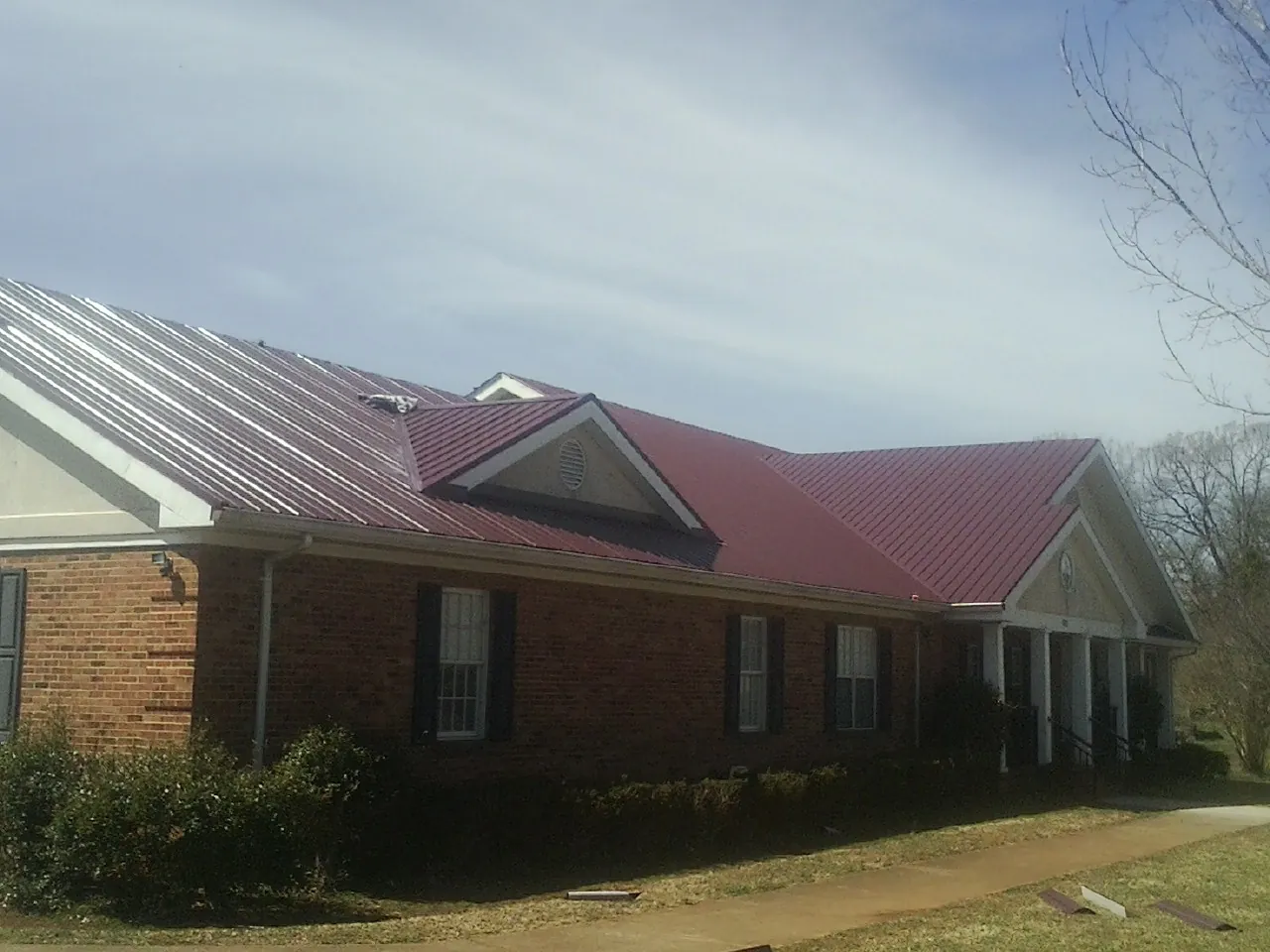 Red metal roof with gabled entries on a long brick building, from a Hail Damage Roof Repair job in Midway