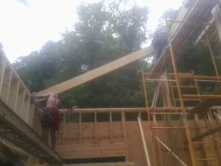 Carpenter raising a rafter beam on a new second story frame in Midway