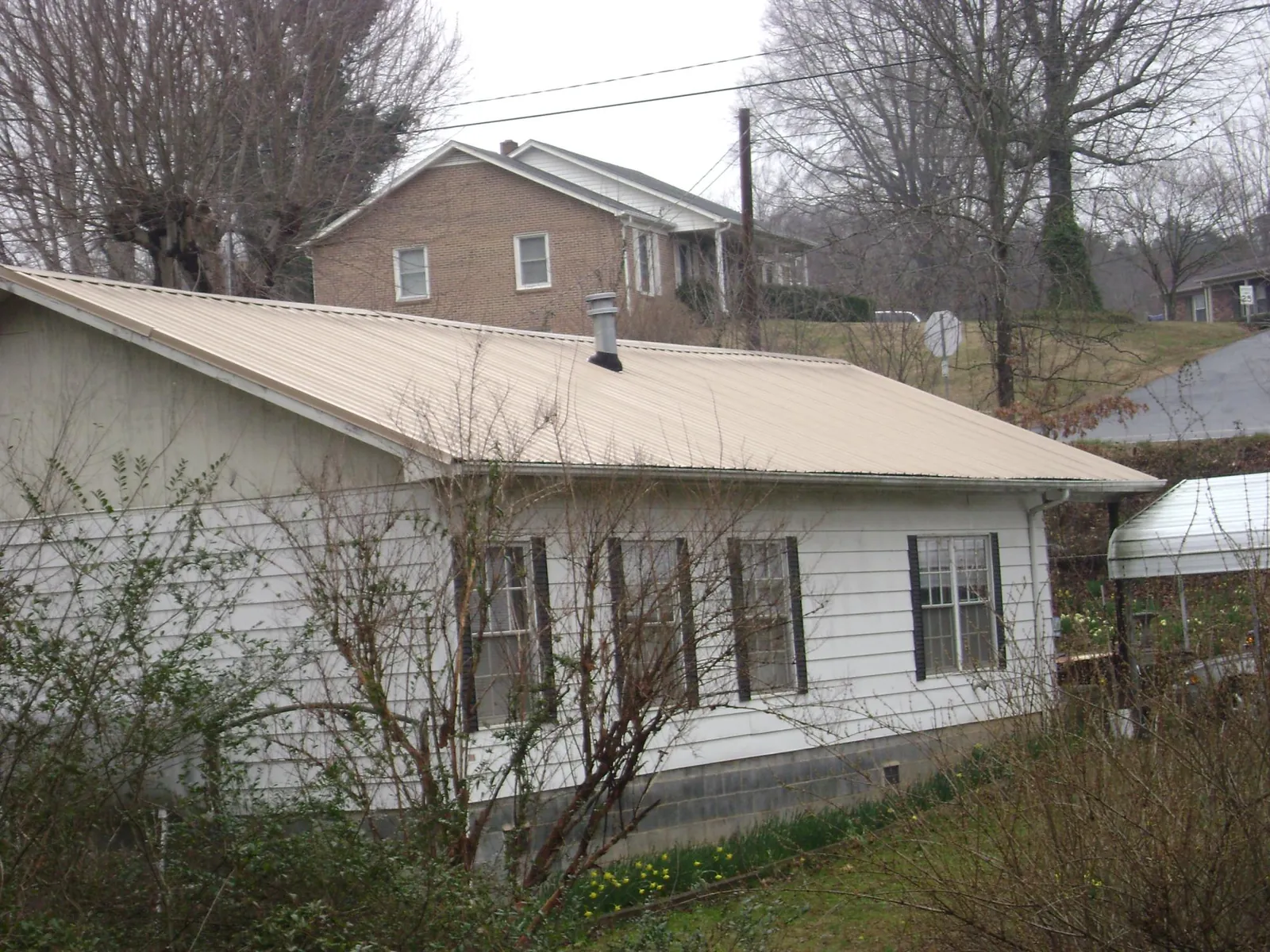Tan metal roof on a white sided house set into a hillside — Commercial Roofing by Roofing Brothers in Midway